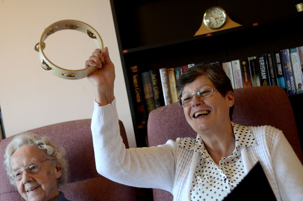 A smiling lady plays a tambourine 