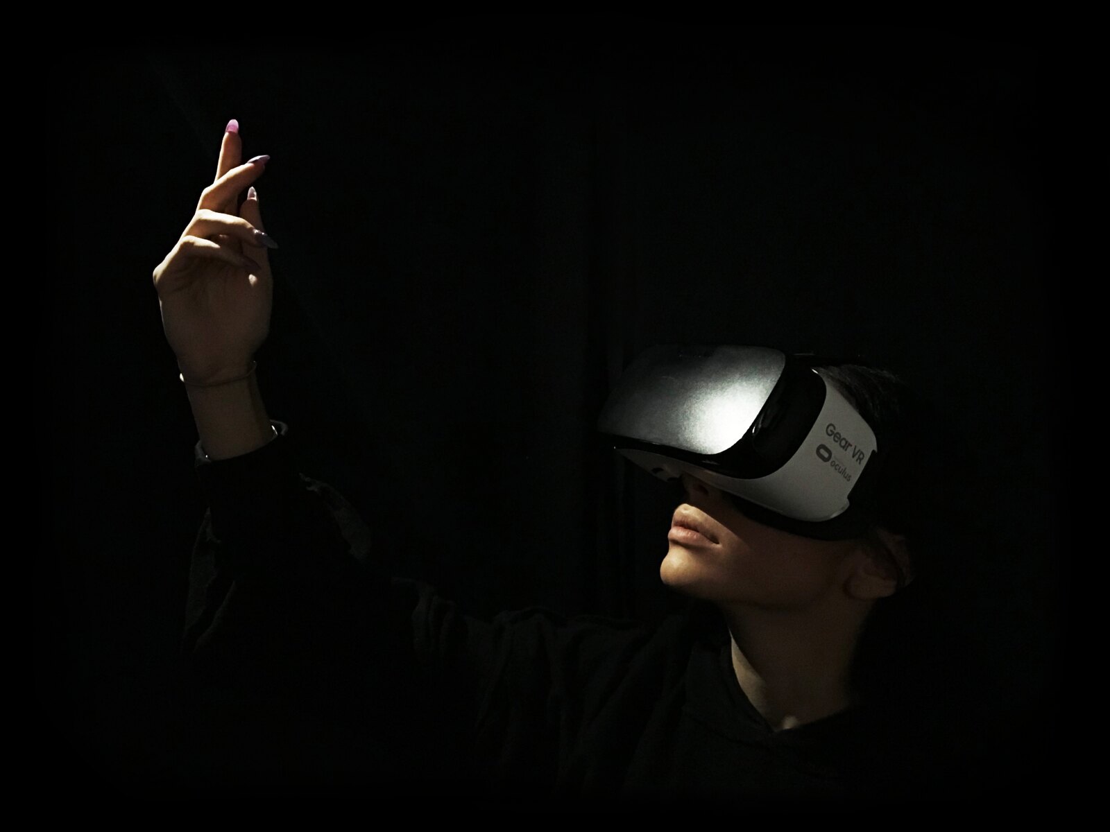 A dancer in a dark room wearing a VR headset raises her arm.