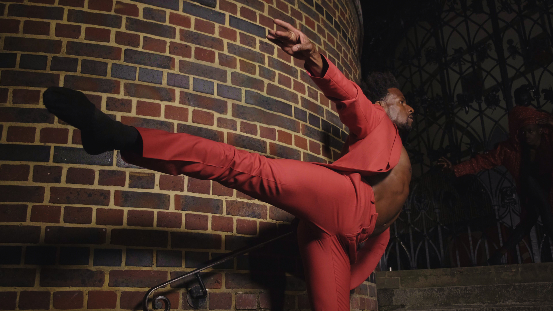 Photograph of a Black ballet dancer wearing red, stood against a wall