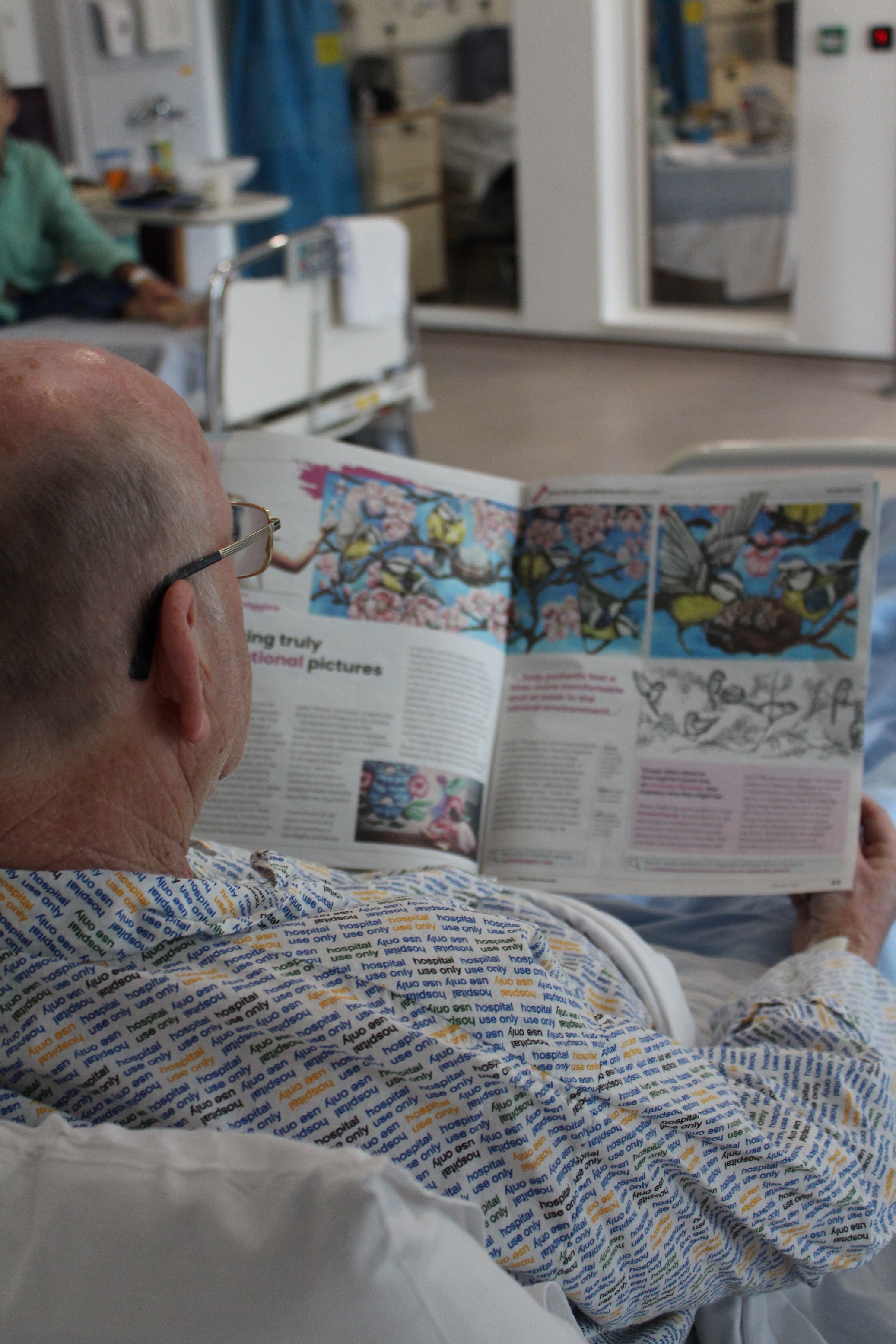 A hospital patient is reading the Boredom Buster Two newspaper on a ward