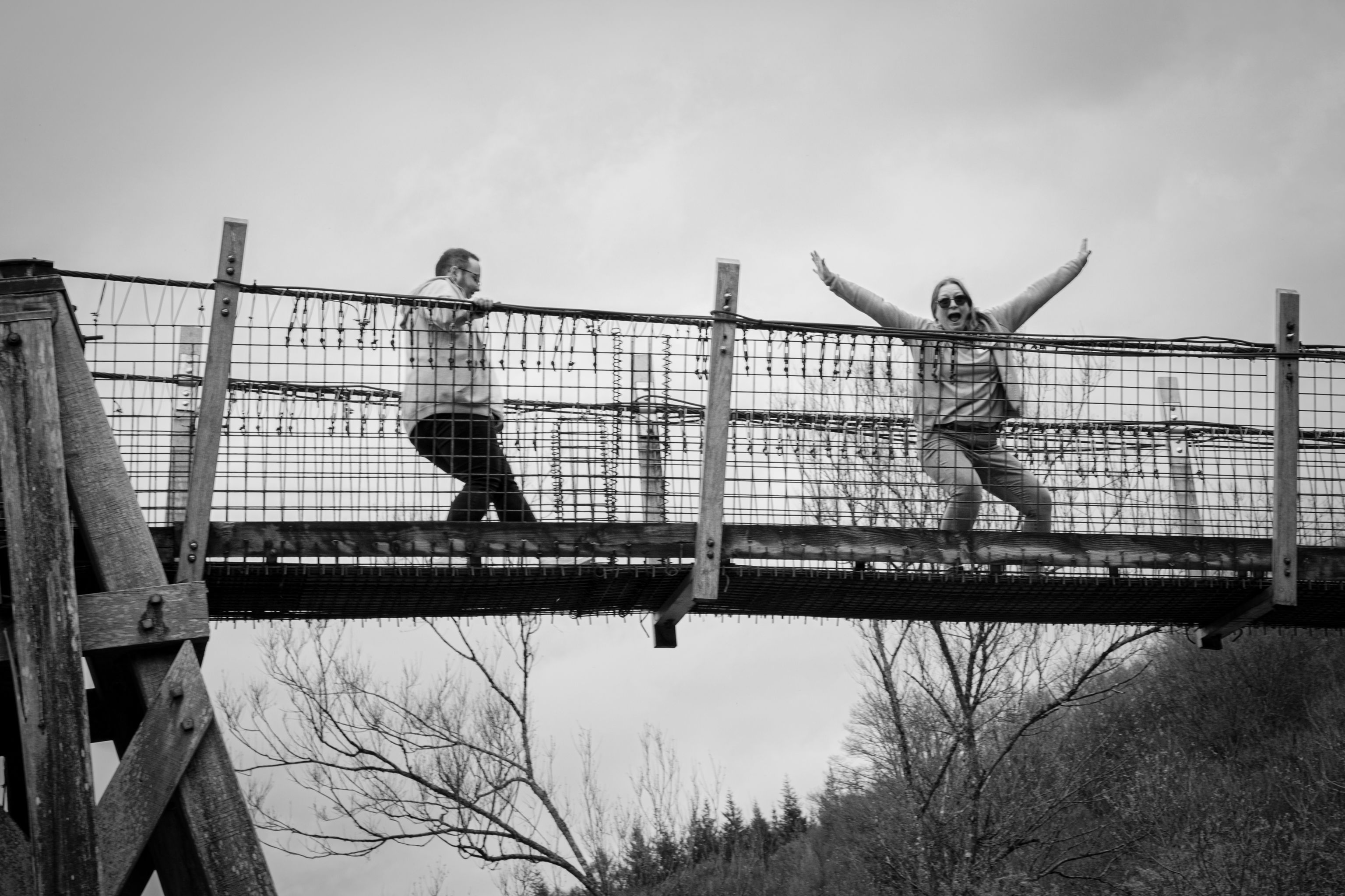 Black and white image of two people stood on a bridge with arms in the air