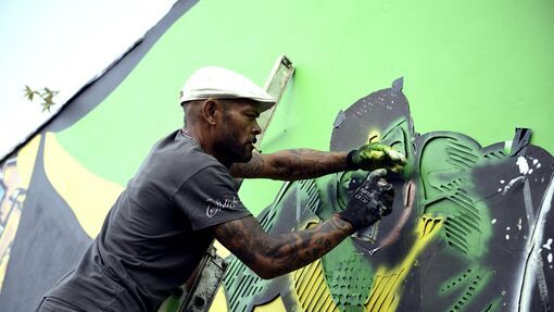 An artist spray paints a mural on a wall.