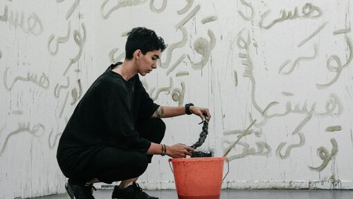 An artist kneels next to an orange bucket in front of a painted mural 